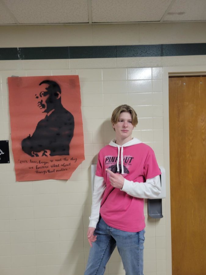 JHS Senior Jorin dresses up with his Pink Out merchandise next to the MLK poster in the JHS hallways.